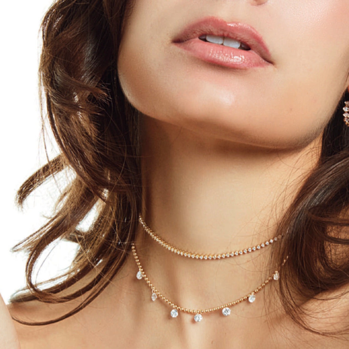 Close-up of seven lab-grown diamonds threaded along a polished 14K yellow gold ball chain necklace by Lumeniri