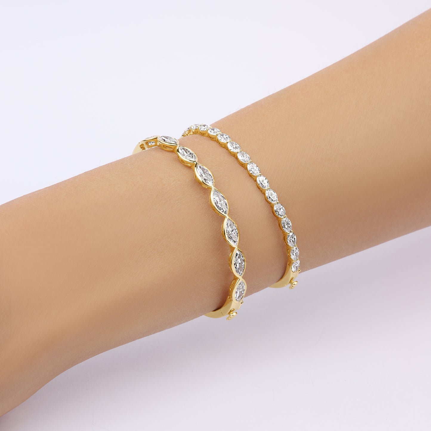 Hand model wearing the Oval Bezel Set East West Tennis Bracelet in 14K yellow gold, showcasing 5.5ct oval-cut lab-grown diamonds set east-west in bezel settings