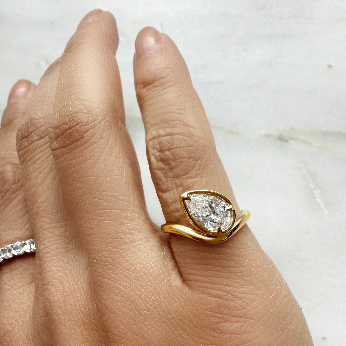 Lumeniri The Calista pinky ring worn on hand, showcasing 1.04ct pear-shaped IGI certified lab grown diamond in sculptural wave bezel setting, elegant modern fine jewelry styling in 14K gold.